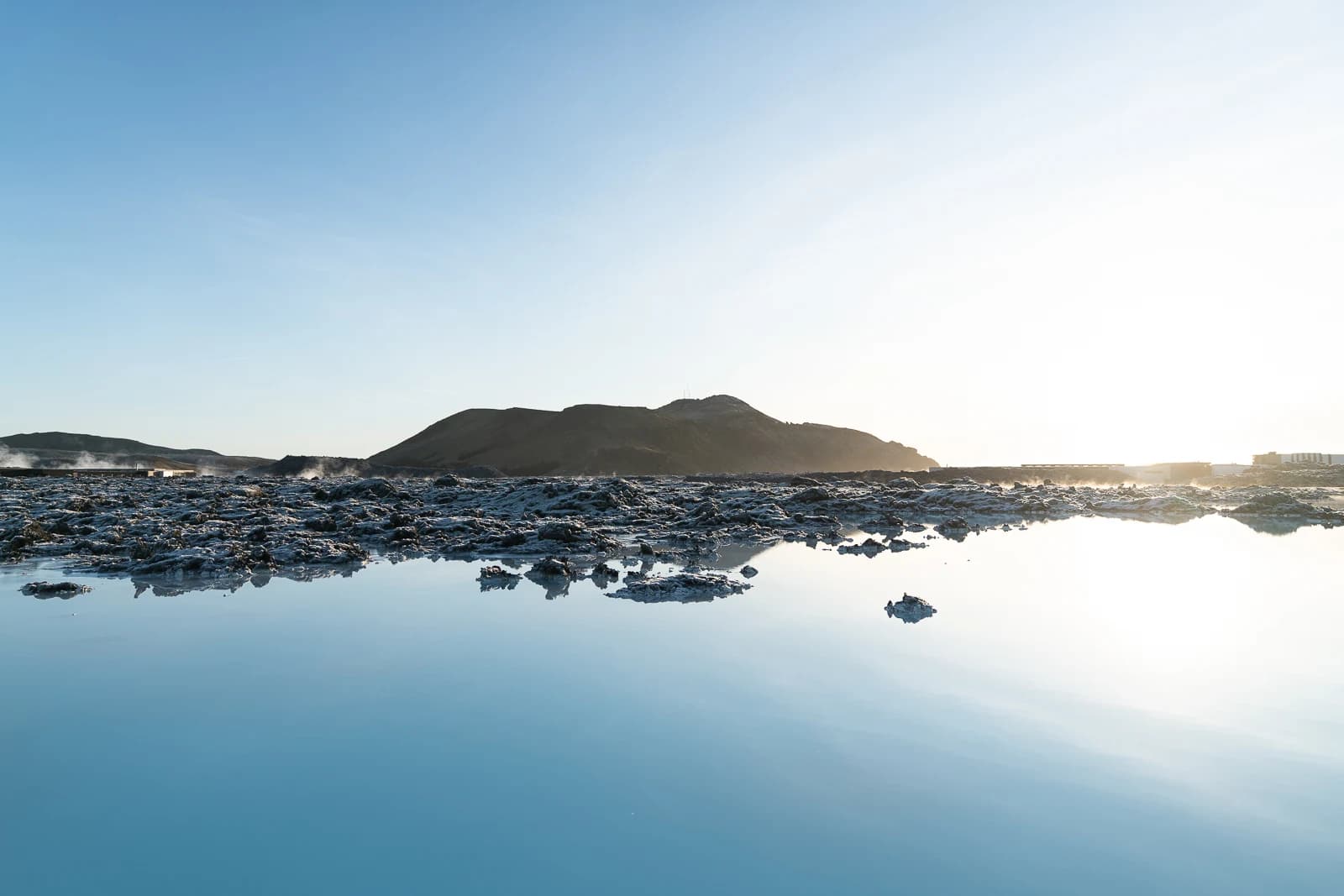 Milky-blue Blue Lagoon water bordered by black Reykjanes lava and low volcanic hills.