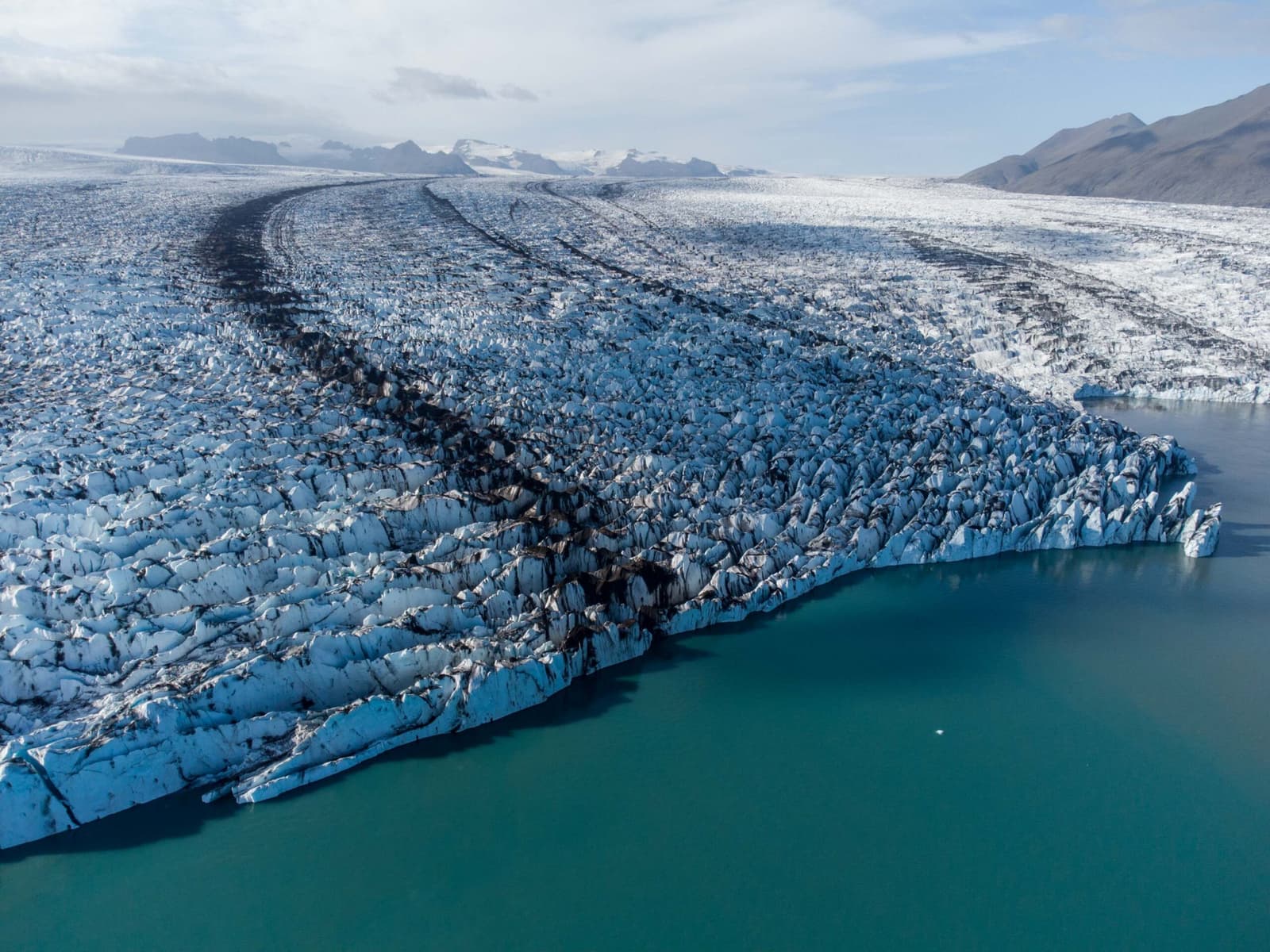 Breiðamerkurjökull glacier calving into a turquoise lagoon with dark moraine bands across the ice.