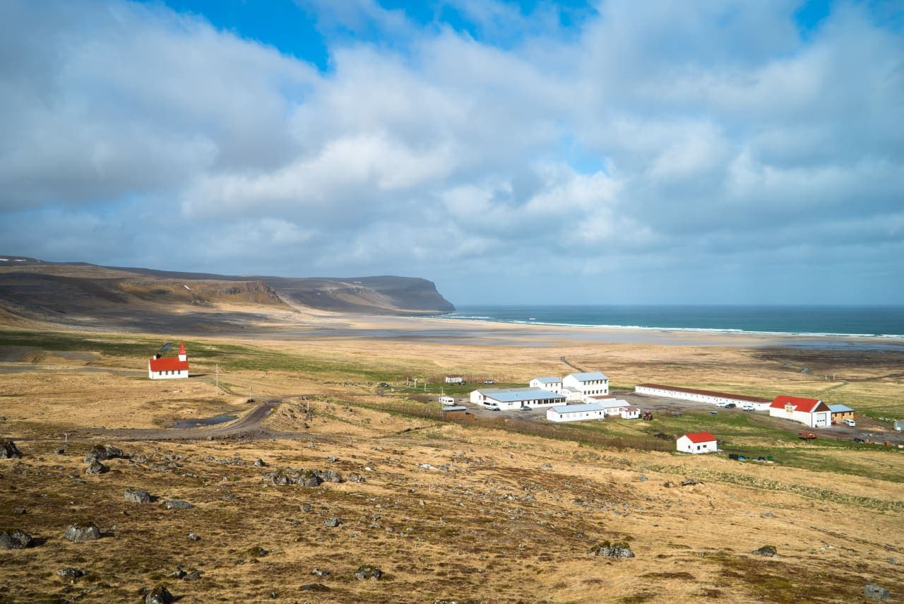 Wide view of Breiðavík beach, church buildings, and surrounding Westfjords slopes.