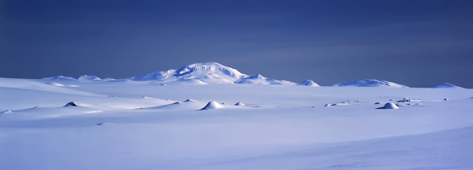 Wide snowy Brúarjökull glacier panorama with dark nunatak peaks and a larger ice-covered mountain in the distance.