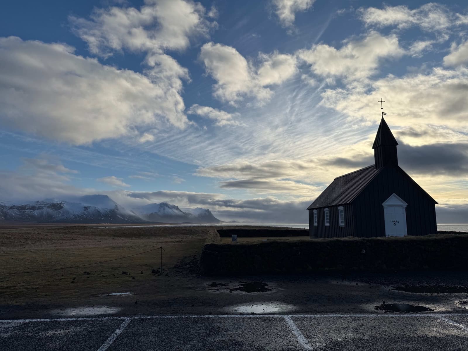 Black Búðakirkja church at Búðir with lava-field ground and Snæfellsnes mountains behind it.