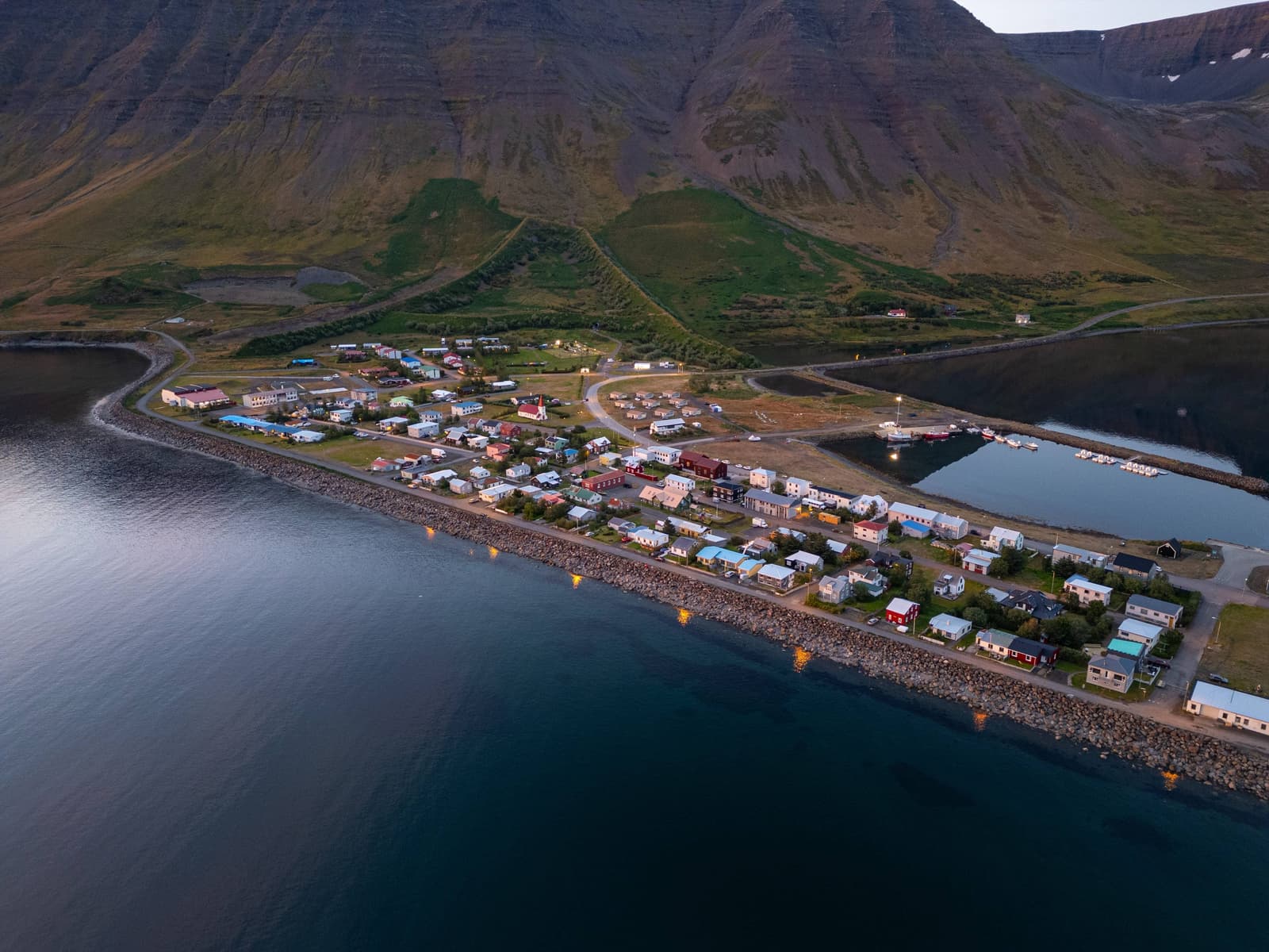 Aerial view of Flateyri village on Önundarfjörður with harbor water and steep Westfjords mountains behind.