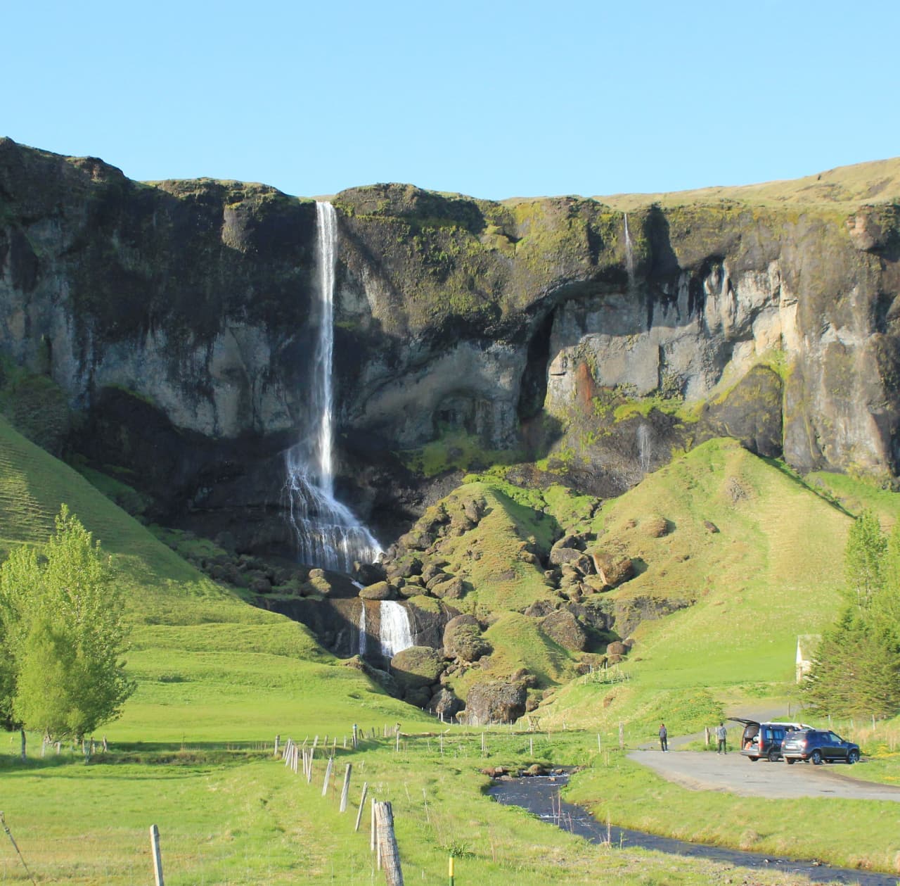 Foss á Síðu falling over green cliffs above farm fields in South Iceland.
