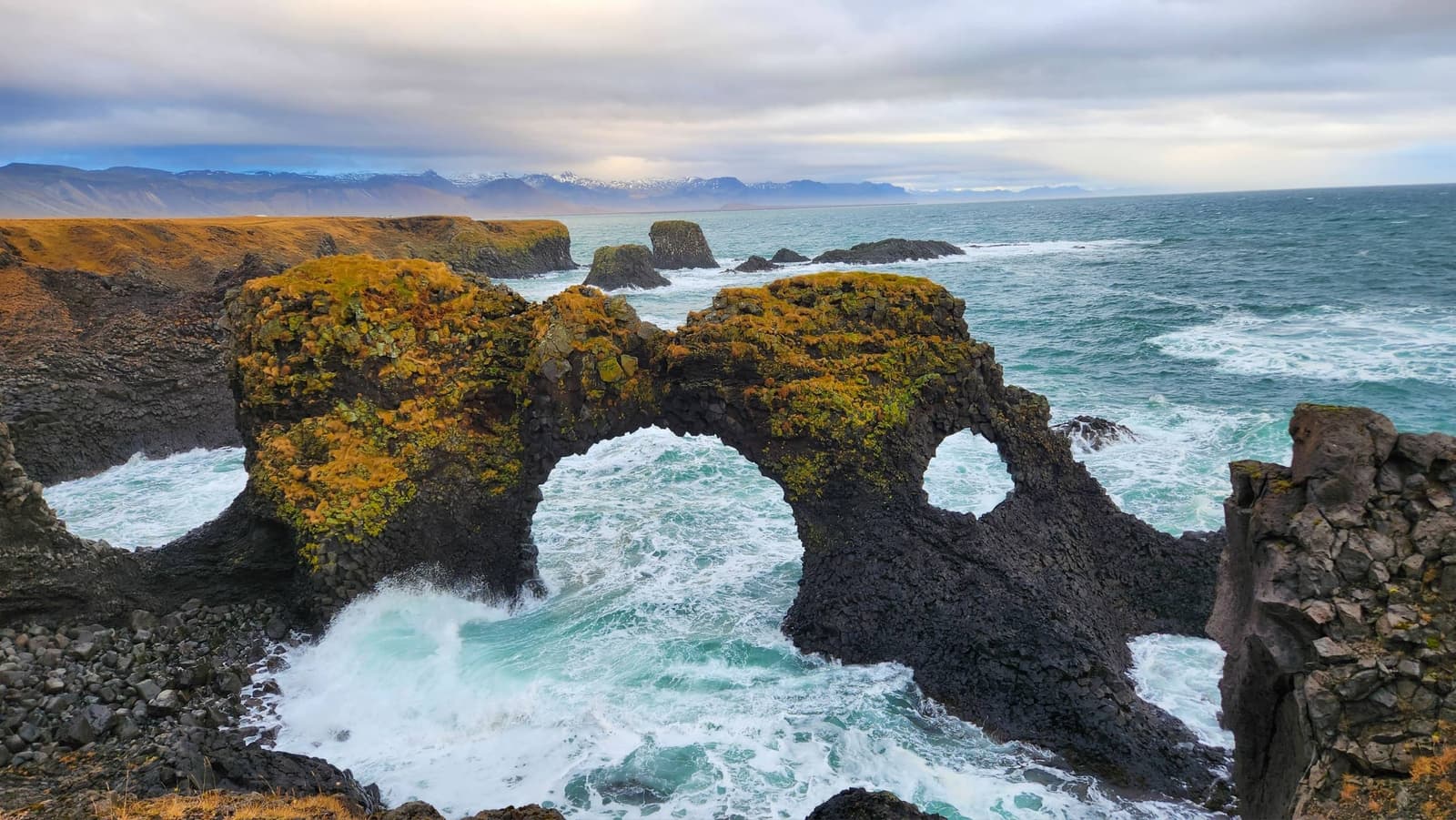 Gatklettur sea arch at Arnarstapi with Atlantic surf breaking through the basalt opening.