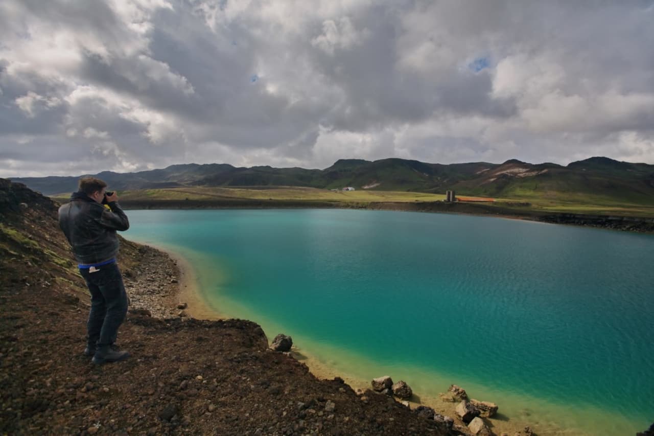 Person photographing the vivid green Grænavatn crater lake on the Reykjanes Peninsula.