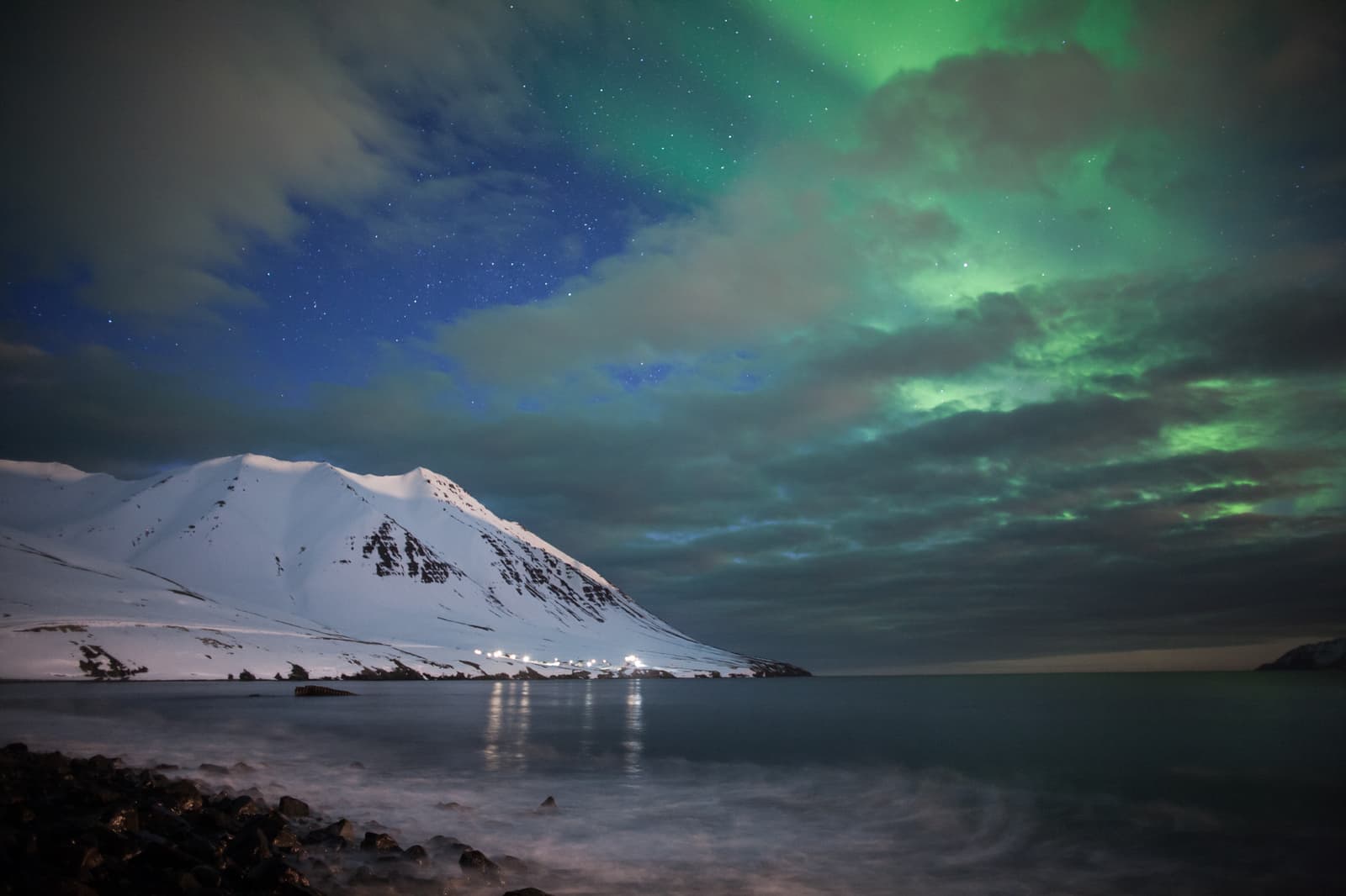 Northern lights over the Grenivík pier with snowy fjord mountains across Eyjafjörður.
