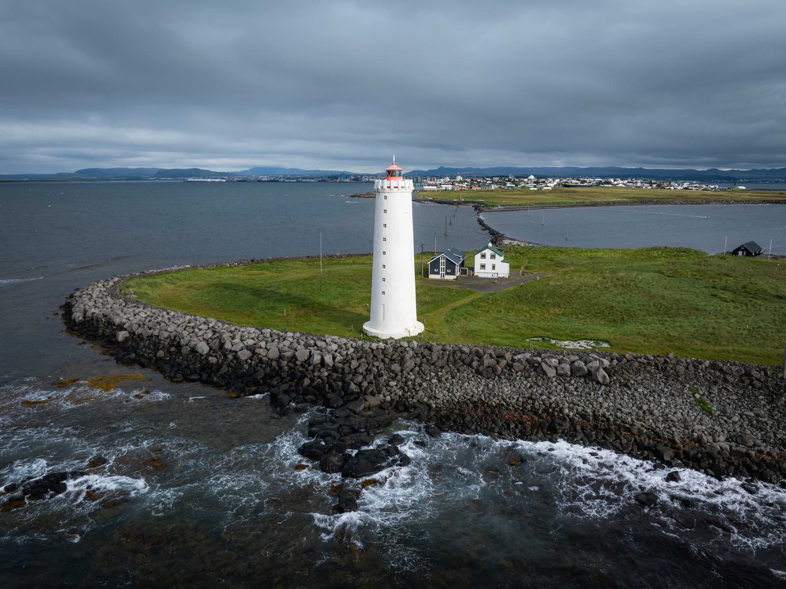 Grótta lighthouse on its tidal islet with Reykjavík and mountains beyond the water
