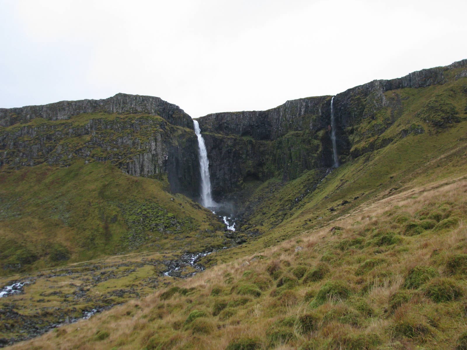 Grundarfoss falling into a grassy basin below dark basalt cliffs near Grundarfjordur on Snæfellsnes.