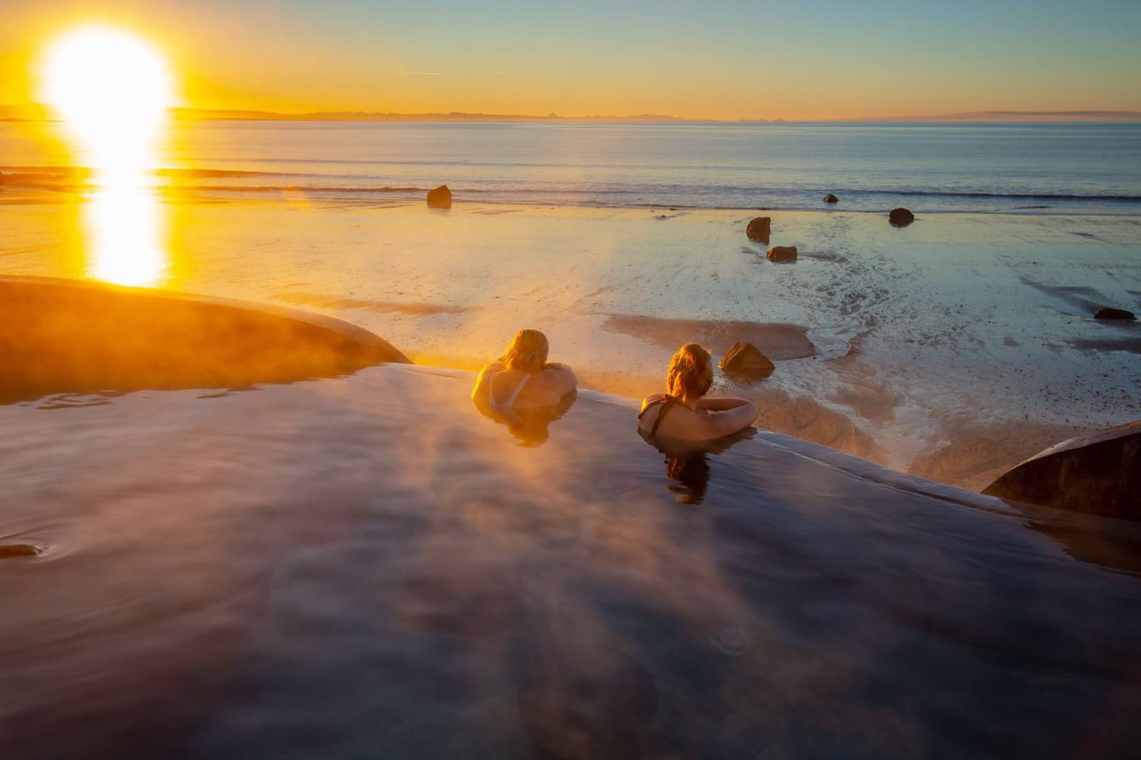 People soaking in Guðlaug hot pool above Langisandur beach and Faxaflói in Akranes.