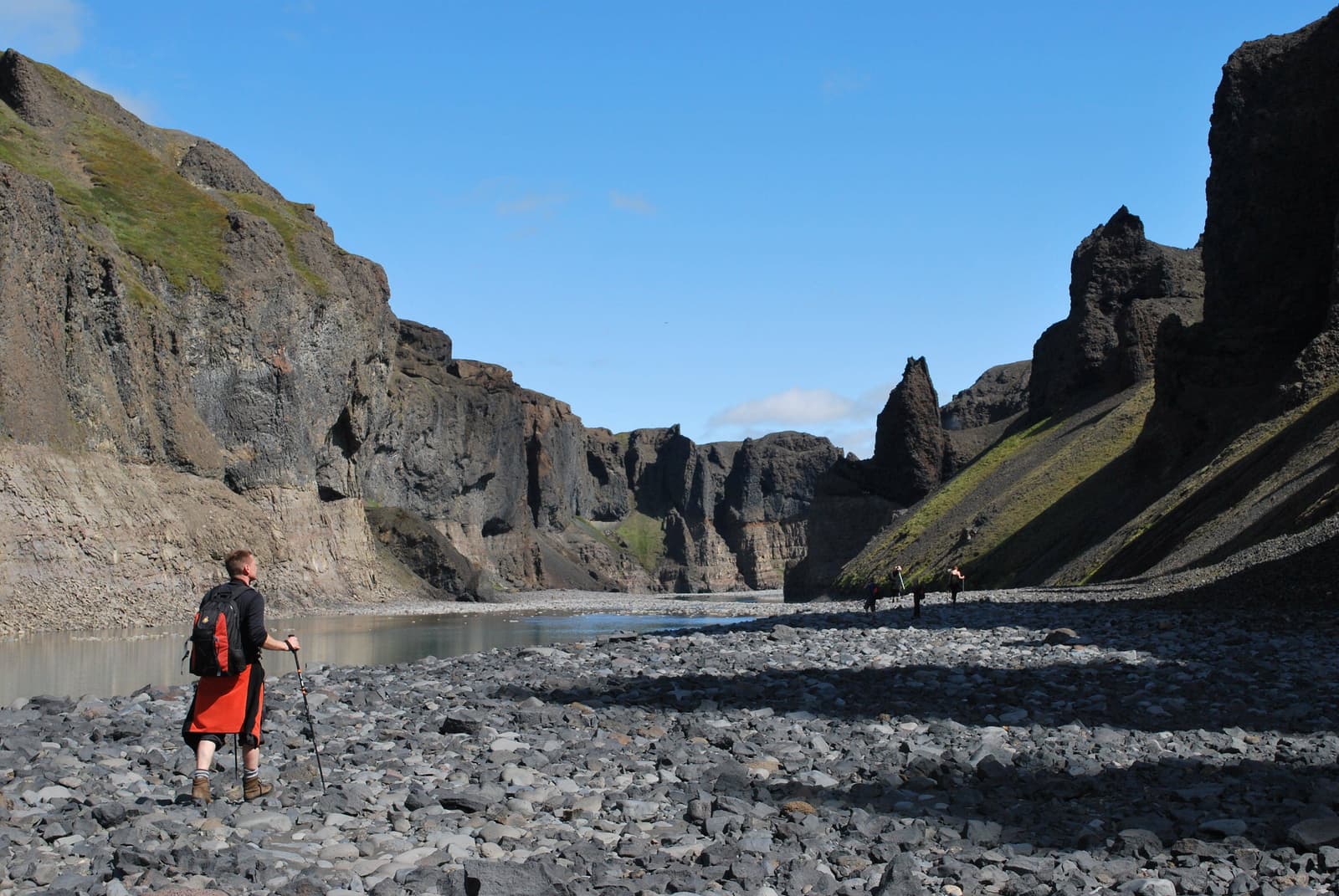 Hiker standing on a viewpoint above the steep dark walls and river of Hafrahvammar Canyon in East Iceland.