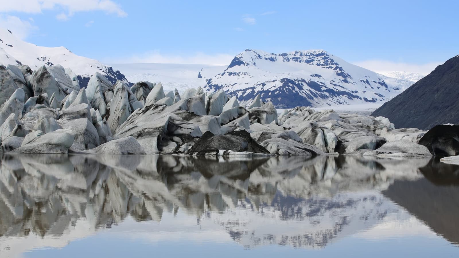 Icebergs and still water at Heinabergslón below snowy mountains in Vatnajökull National Park.