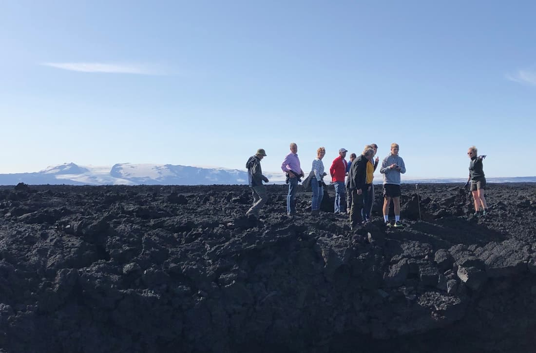 Visitors walk beside rough black lava on the waymarked trail at Holuhraun with Vatnajökull in the distance.