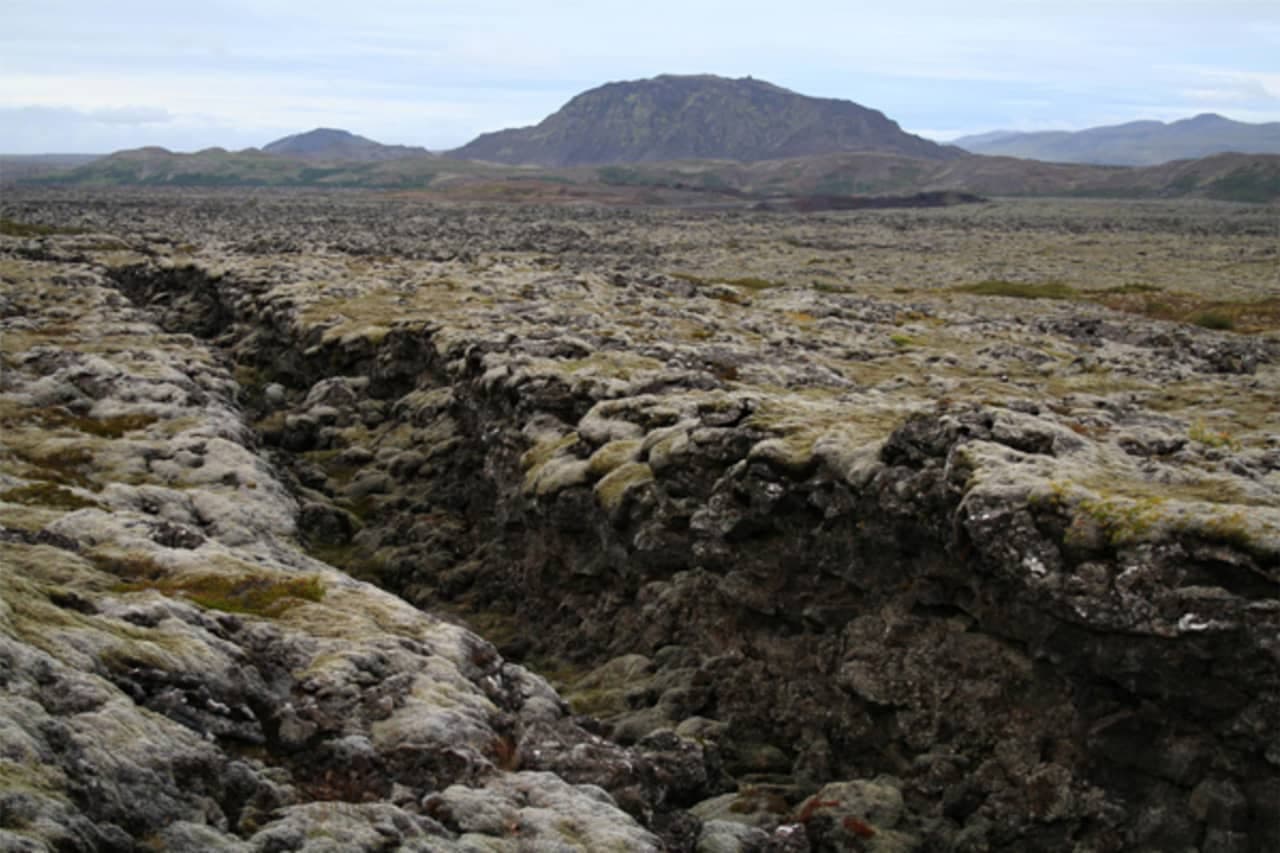 Kapelluhraun lava field near Hafnarfjörður with rough mossy rock and low hills beyond.