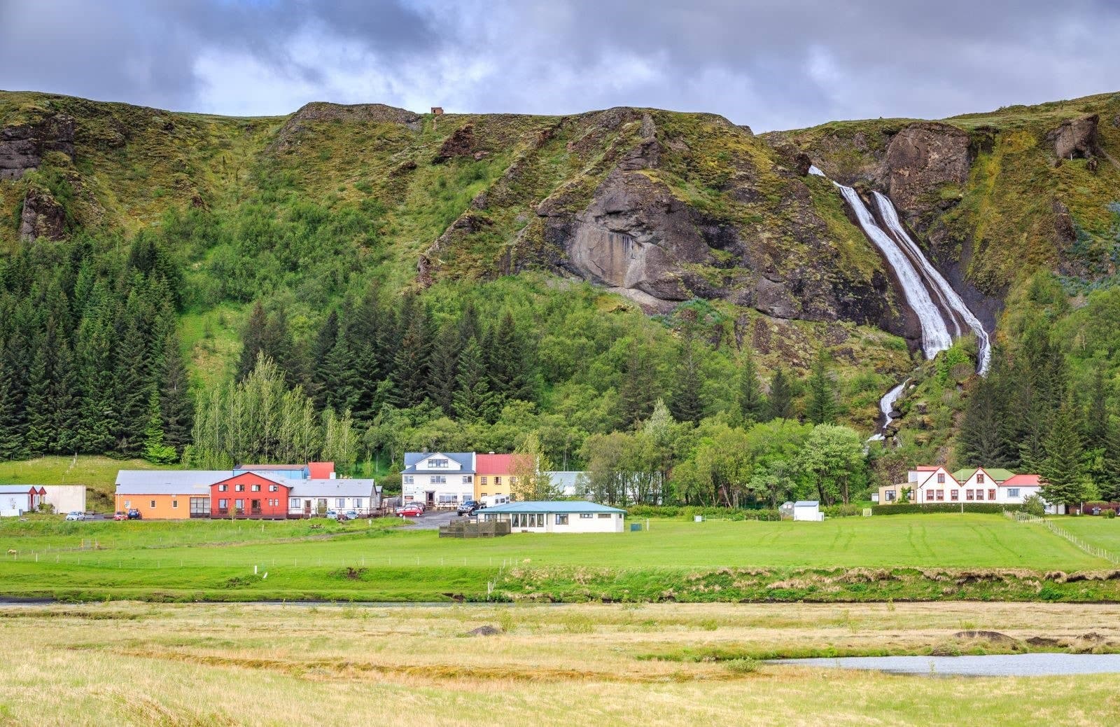 Kirkjubæjarklaustur village below green cliffs with Systrafoss dropping behind the houses.