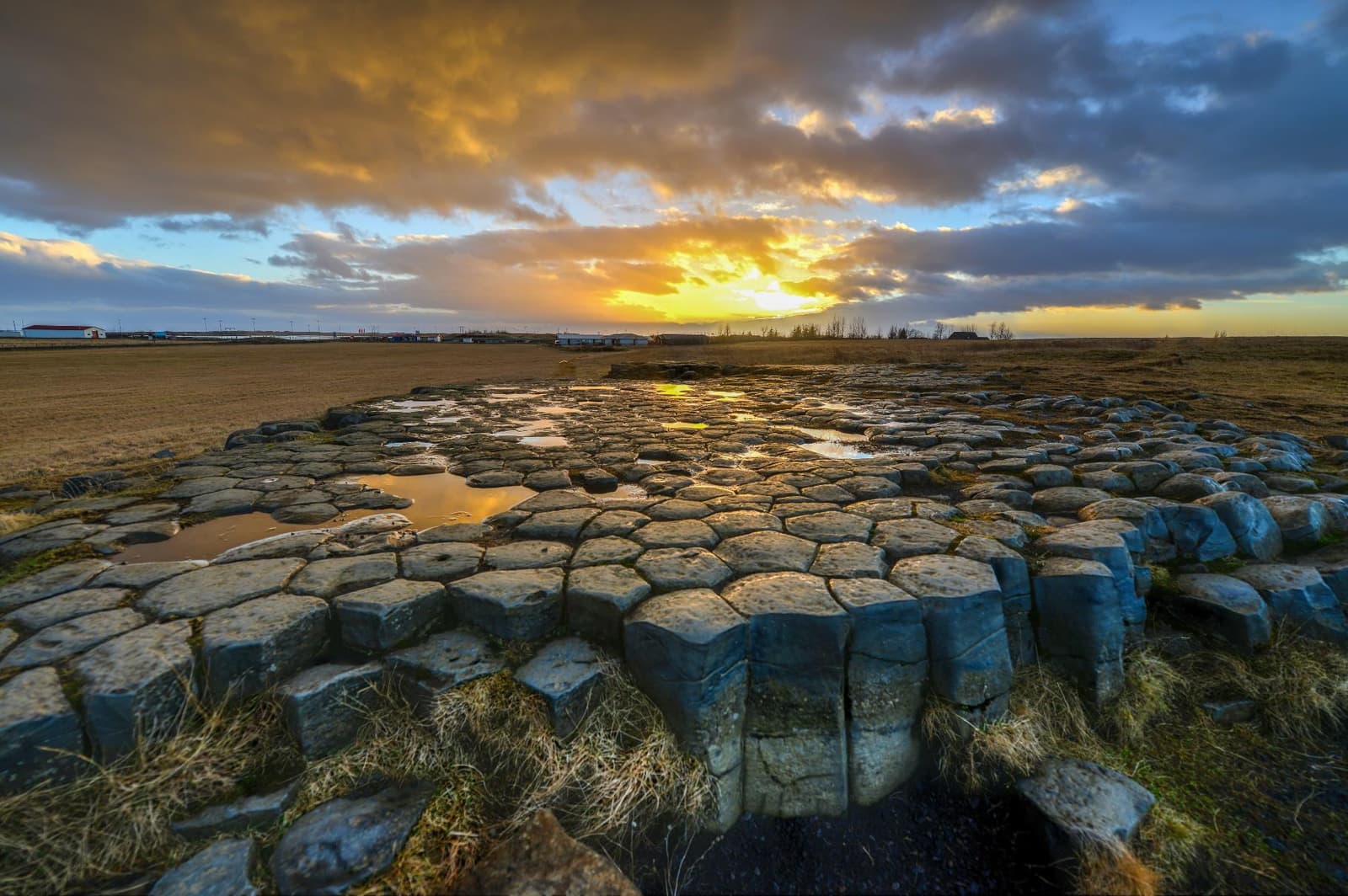 Kirkjugólf's protected basalt pavement stretching across the grass with sunset light and open South Iceland fields beyond.