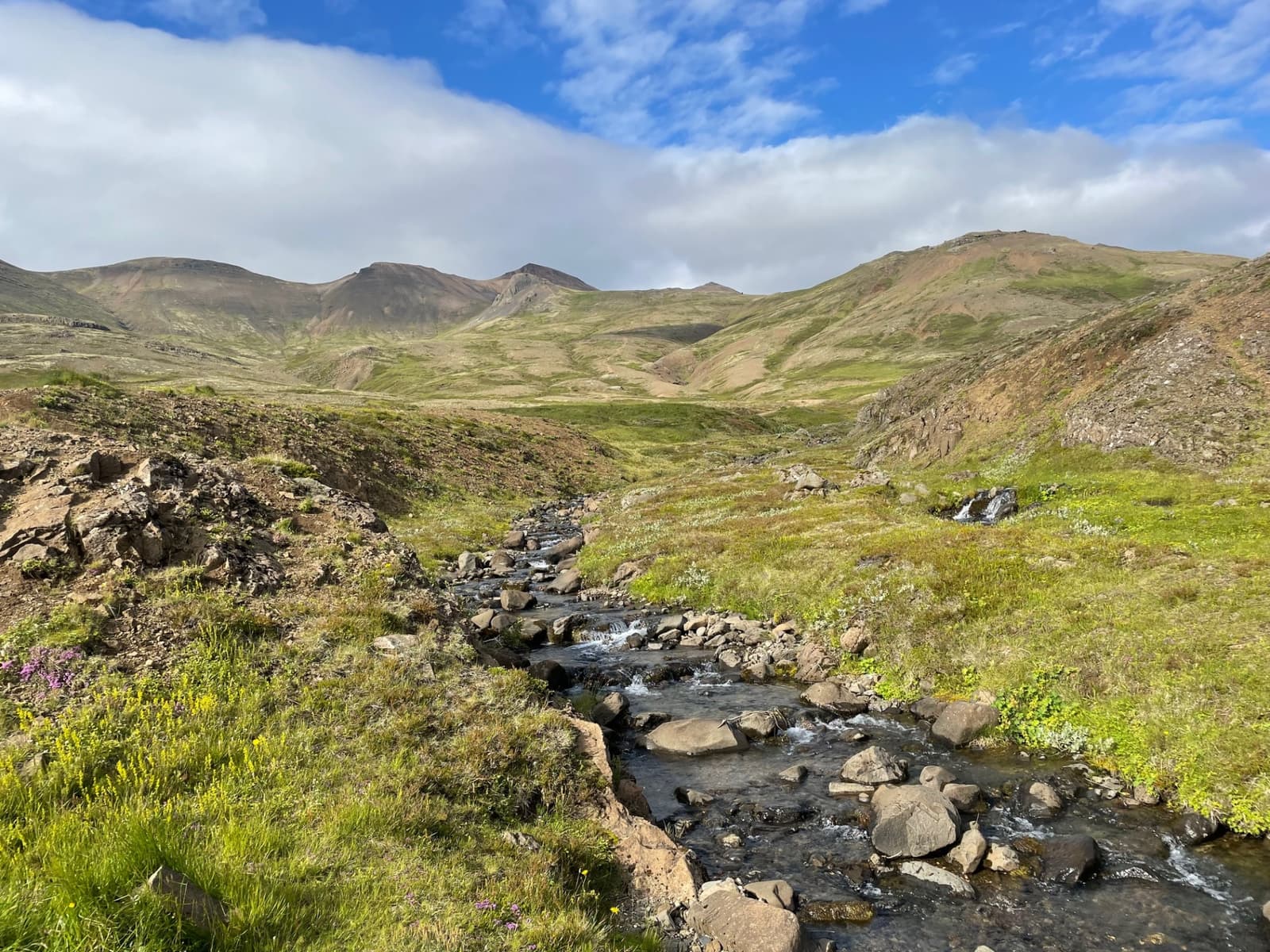 The Skarðsá stream valley below Móskarðshnjúkar with rhyolite slopes and rocky hiking terrain.
