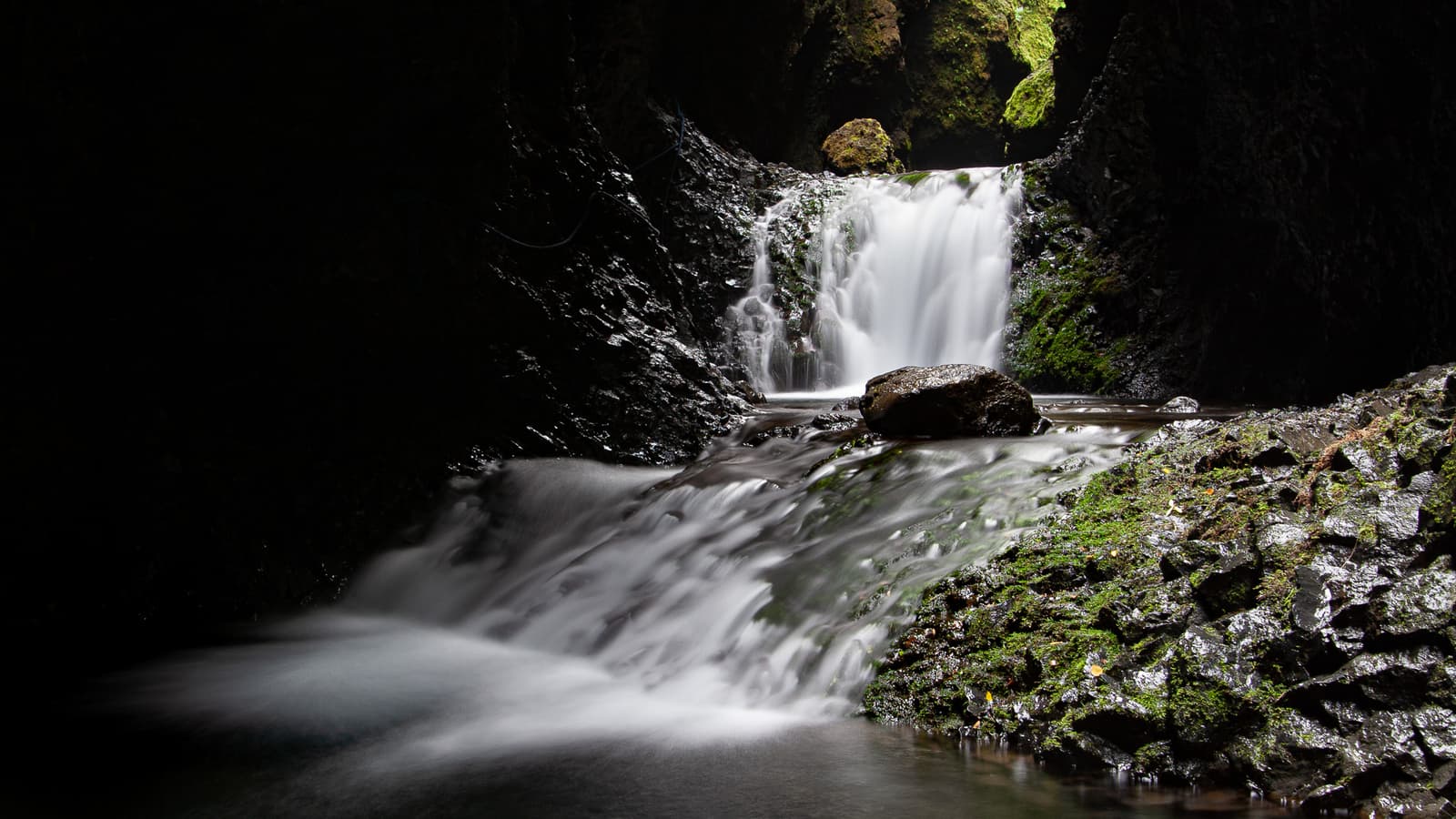 Dark mossy Nauthúsagil ravine with water flowing through the narrow canyon.