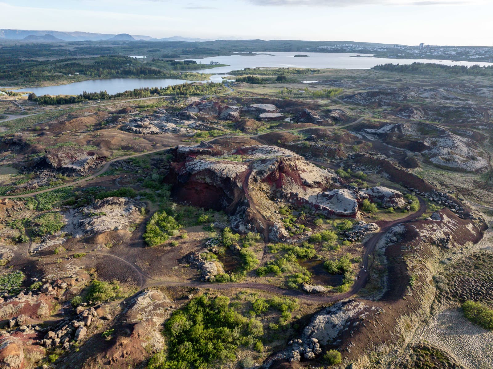 Red and dark Rauðhólar pseudocraters, paths, Elliðavatn, and Reykjavík suburbs from above.