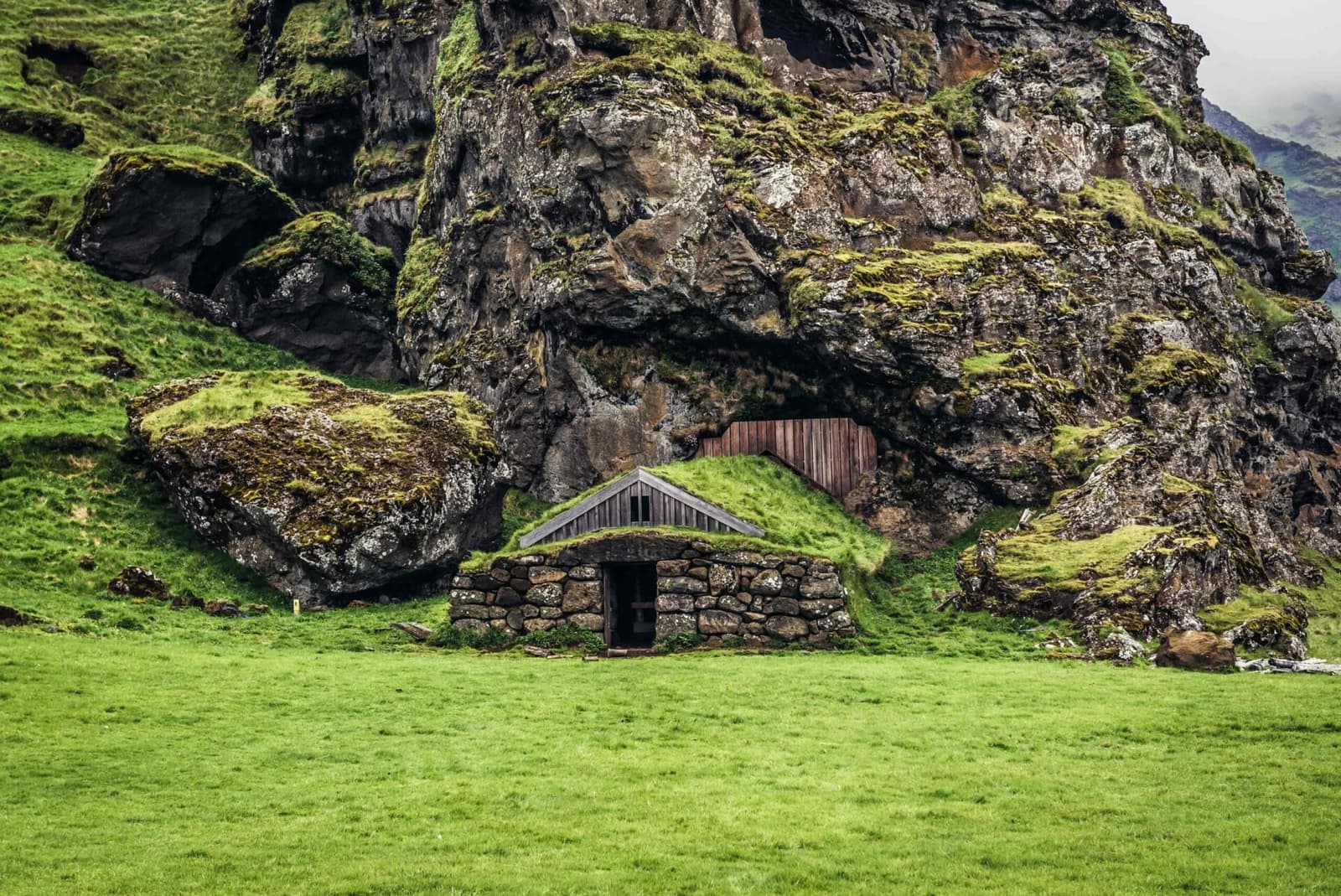 Rútshellir cave entrance and its turf-fronted sheep house beneath the rock wall under Eyjafjöll.