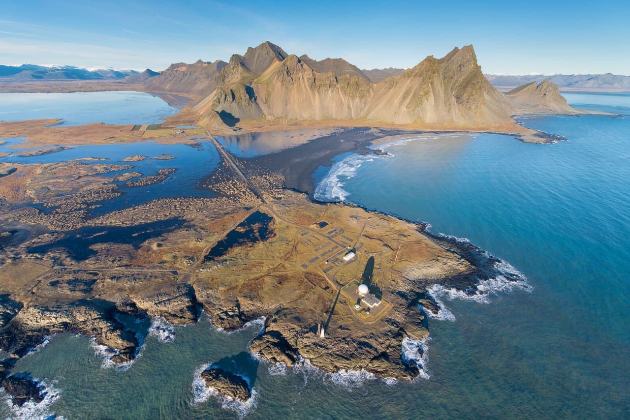 Aerial view of Stokksnes peninsula, Vestrahorn mountain, black sand, shoreline, and radar buildings in southeast Iceland.