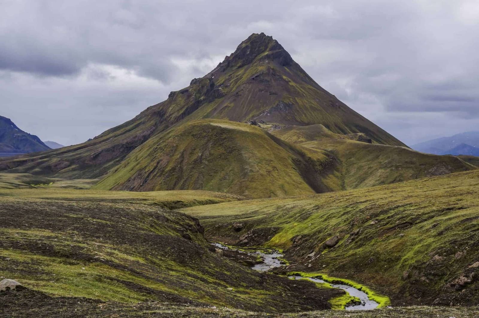 Stórasúla rising as a green cone above a stream and dark Highland slopes near Hvanngil.