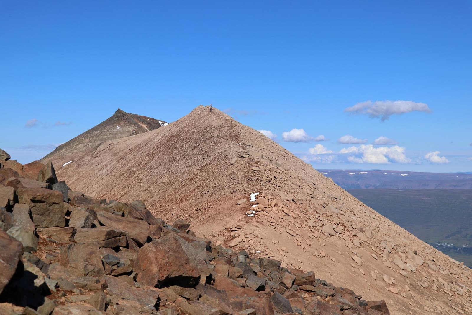 Two pale rhyolite peaks of Súlur above Akureyri with rocky foreground and blue sky.