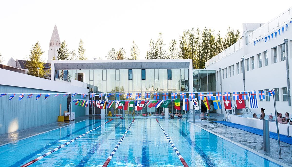 Outdoor lanes at Sundhöllin in central Reykjavík with flags above the pool and a Hallgrímskirkja spire in the background.