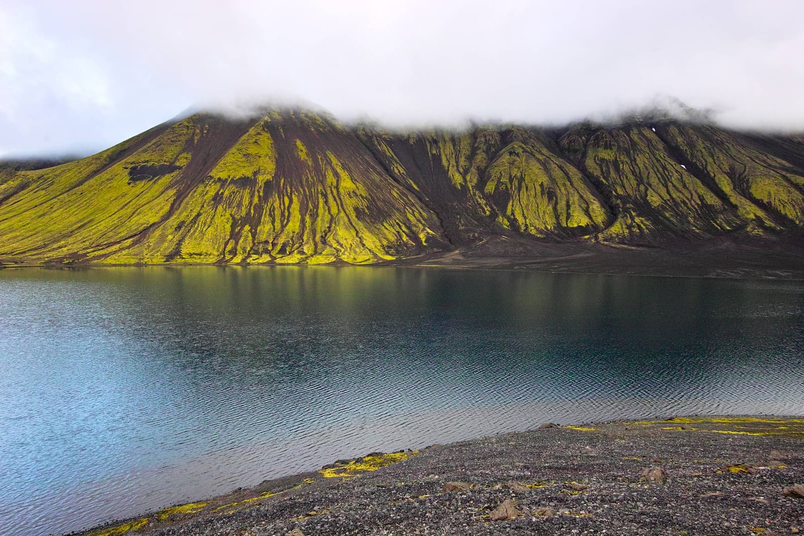 Sveinstindur mountain rising above Langisjór with low cloud over green and black slopes.
