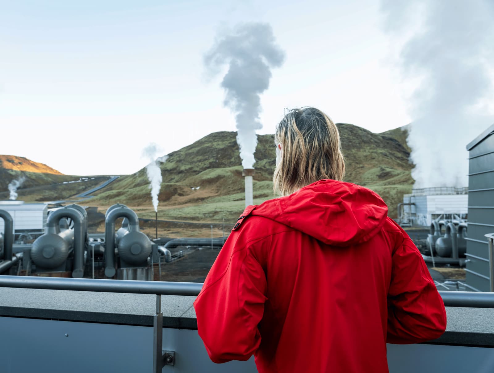 Steam rising beside Hellisheiði Power Plant below green hills at The Geothermal Energy Exhibition.