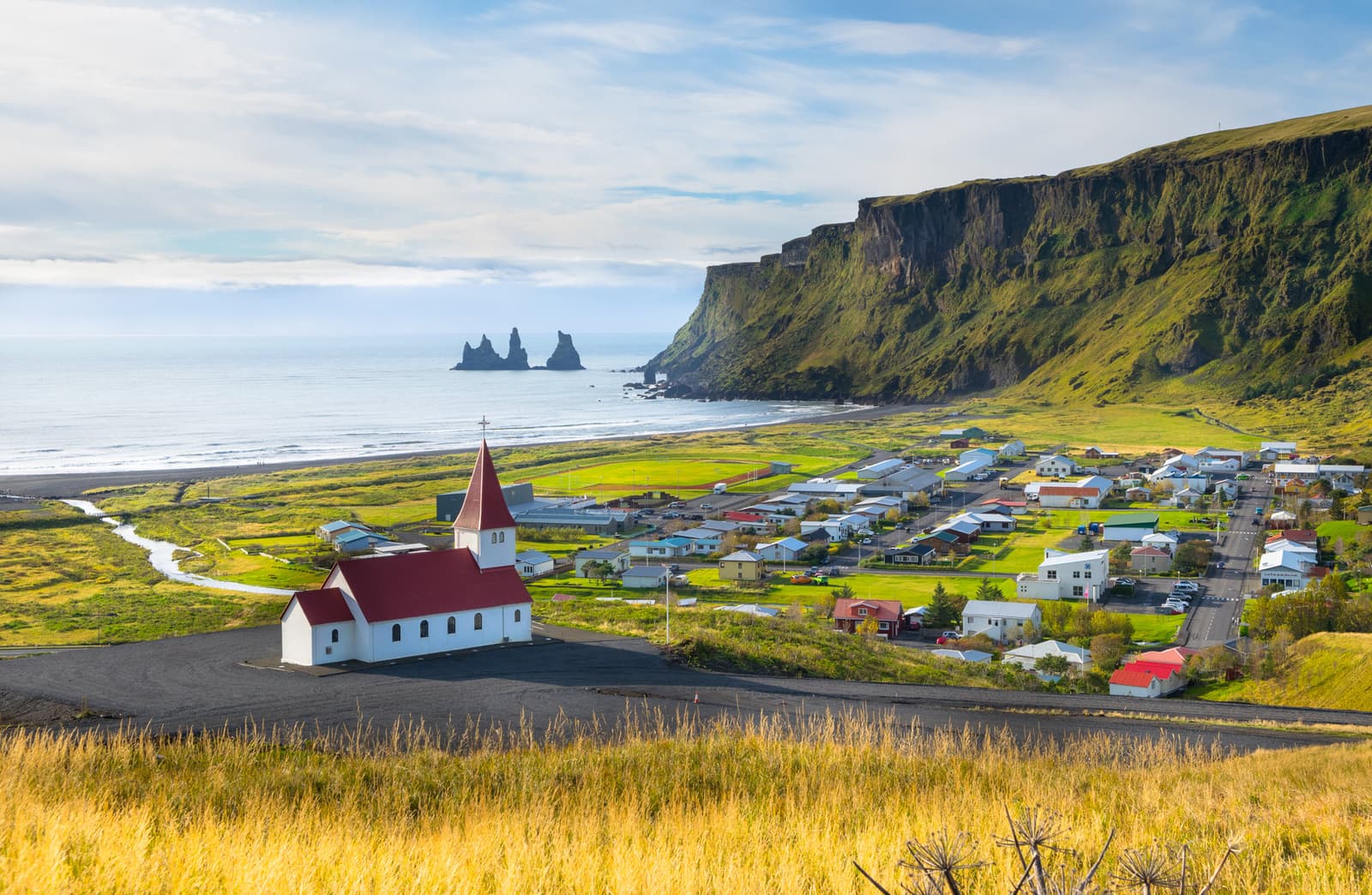 Vík village with Víkurkirkja, black-sand coast, and Reynisdrangar in the distance.
