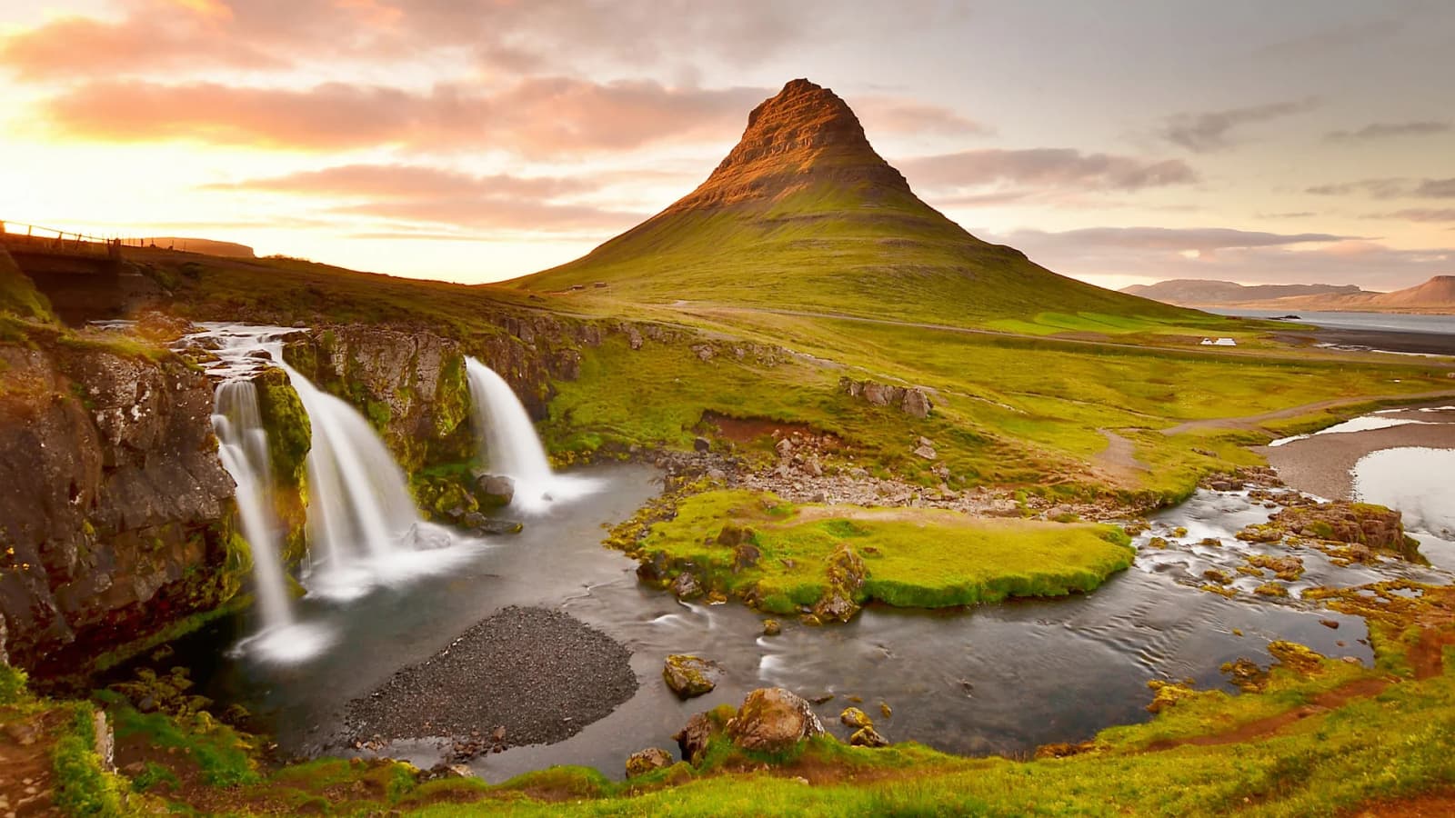 Kirkjufell mountain and Kirkjufellsfoss waterfalls beneath a warm evening sky.