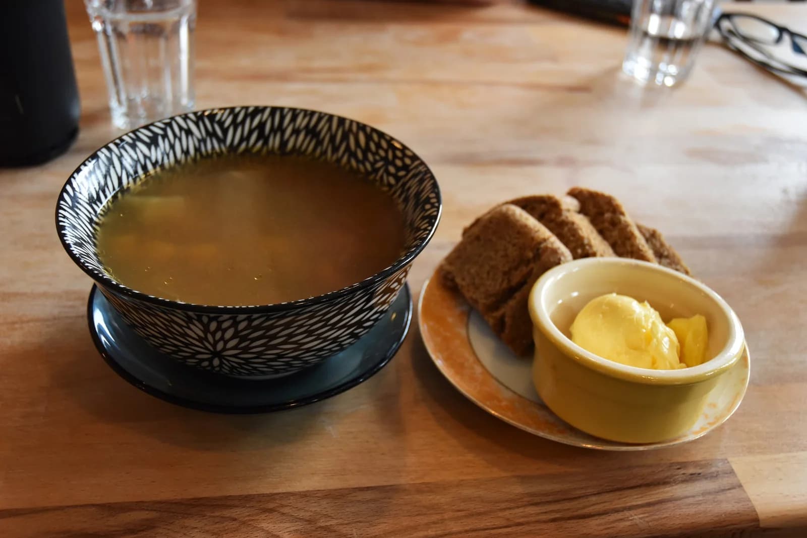 A bowl of soup with bread and butter on a restaurant table.