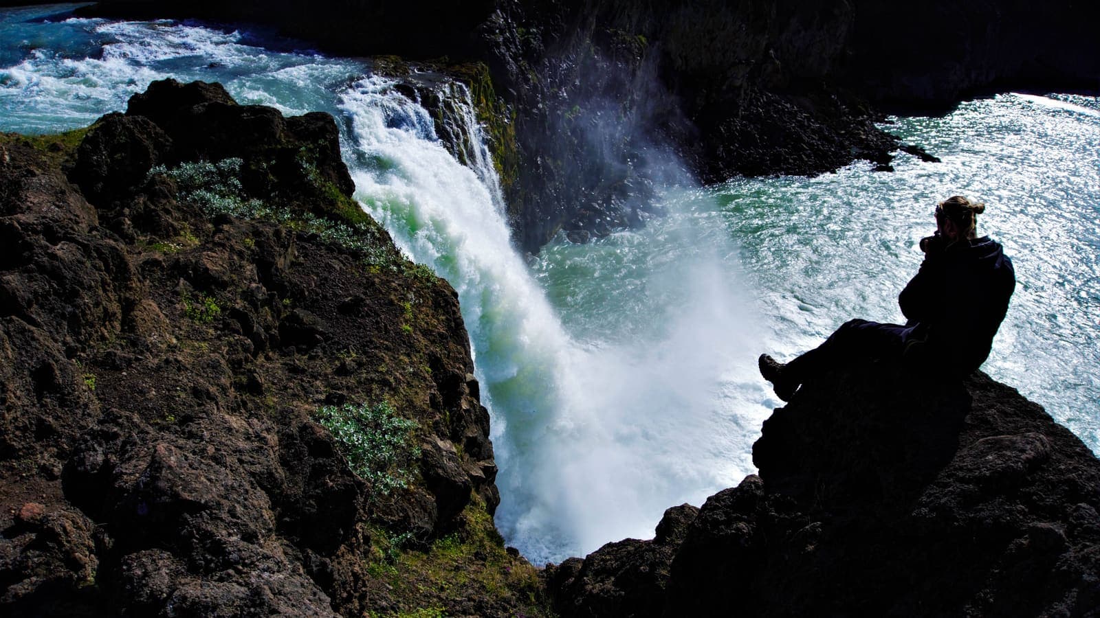 Photographer sitting on rocks while taking pictures of an Icelandic waterfall