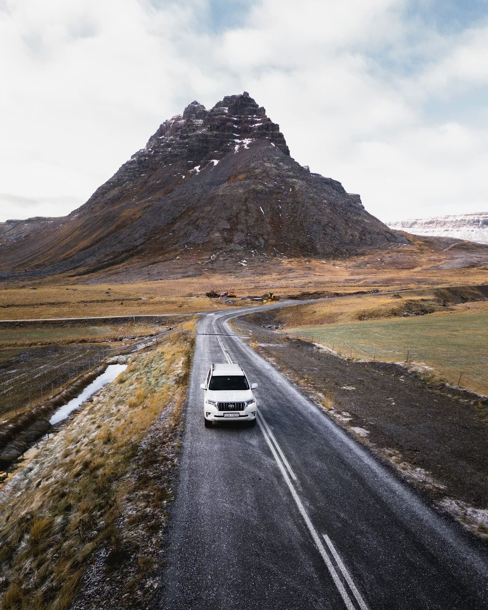 Vehicle driving on an Iceland winter road below a steep mountain.