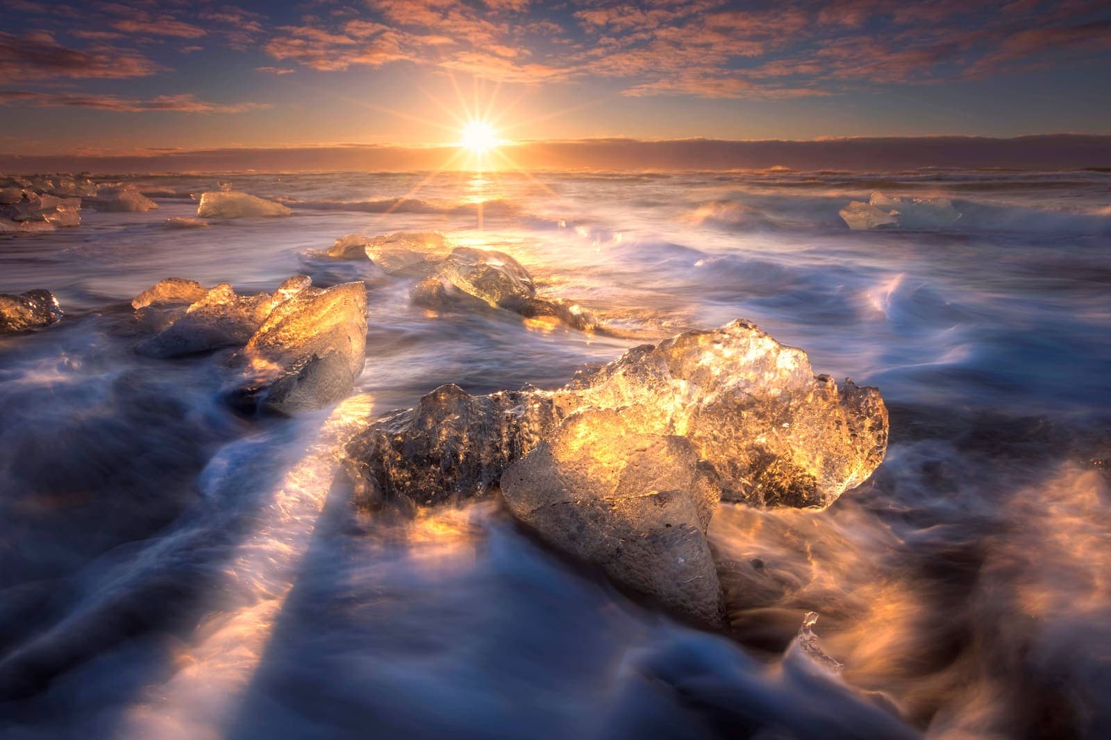 Glacier ice scattered across black sand at Diamond Beach under low golden light.