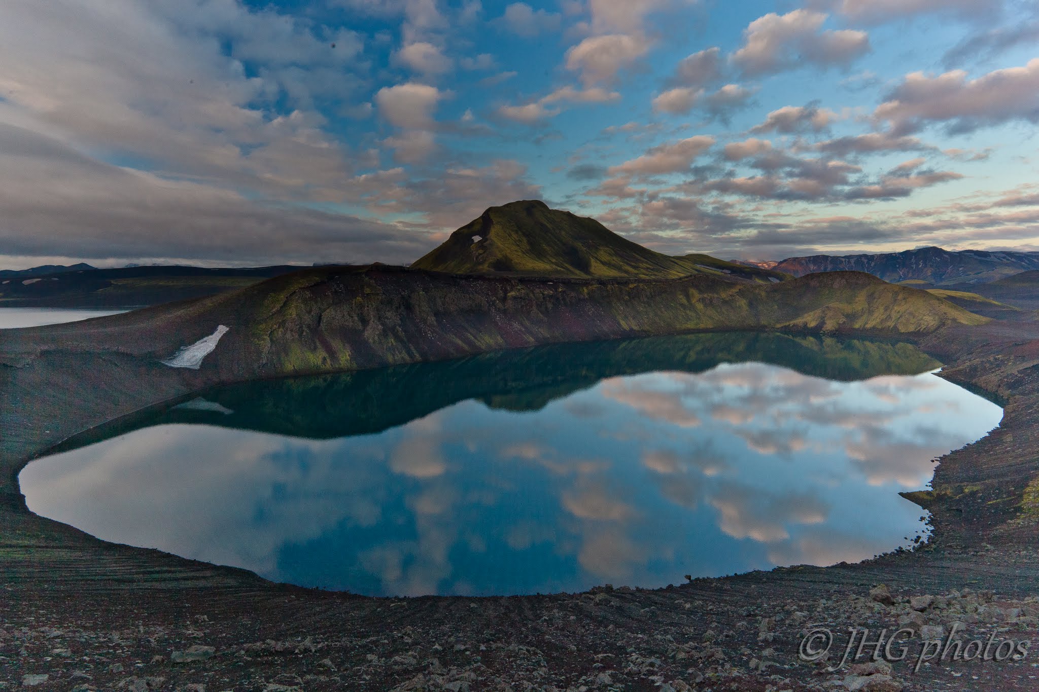 Hnausapollur crater lake seen from the rim with dark rock and green moss around the water.