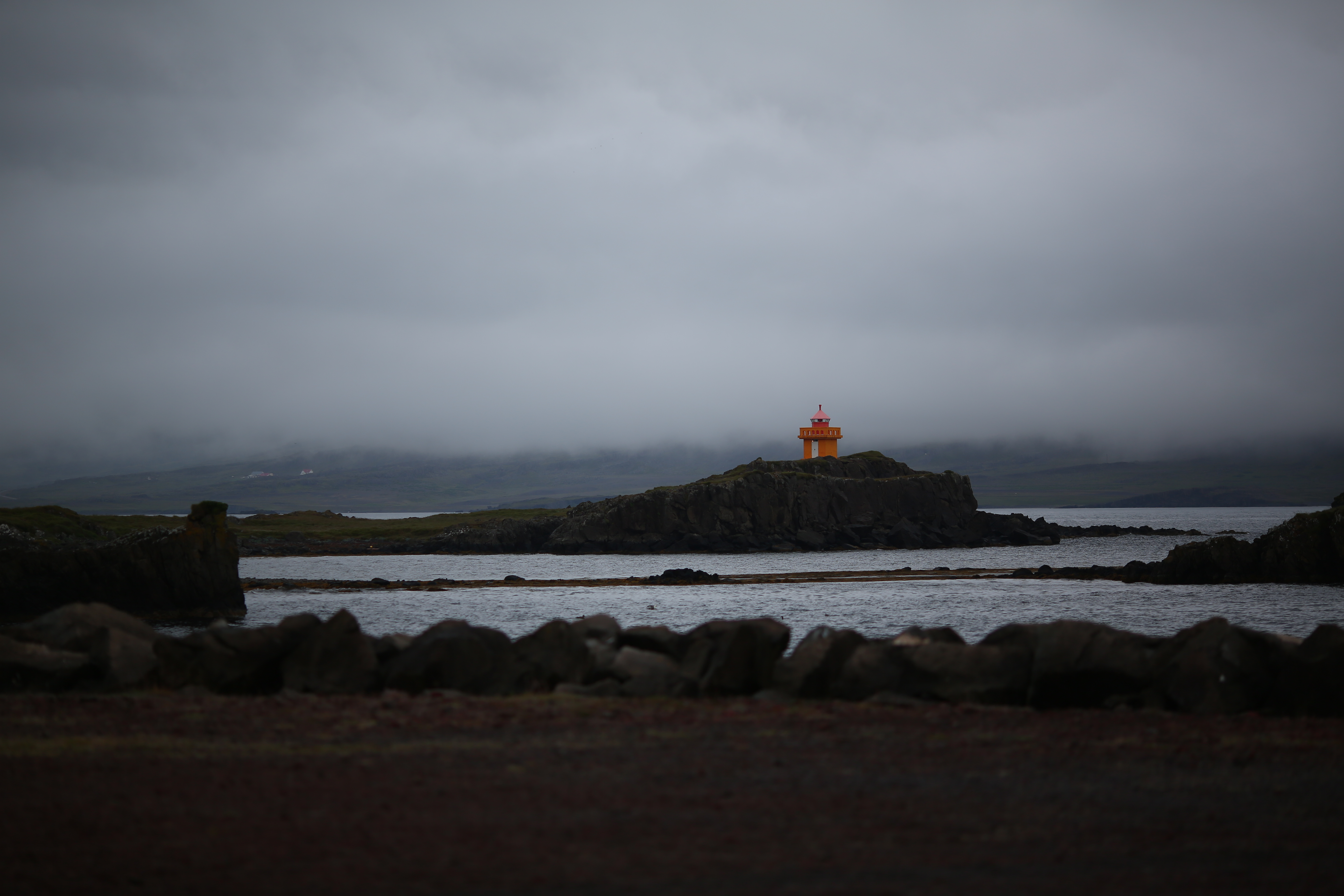 Djúpivogur Lighthouse on a grassy slope with East Iceland shoreline behind it.