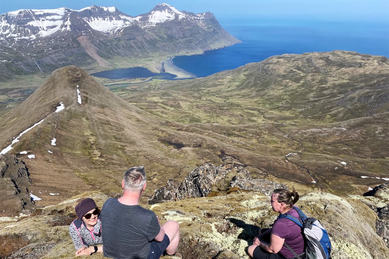 Hikers resting above Vöðlavík with Gerpir-area mountains and coastline below.