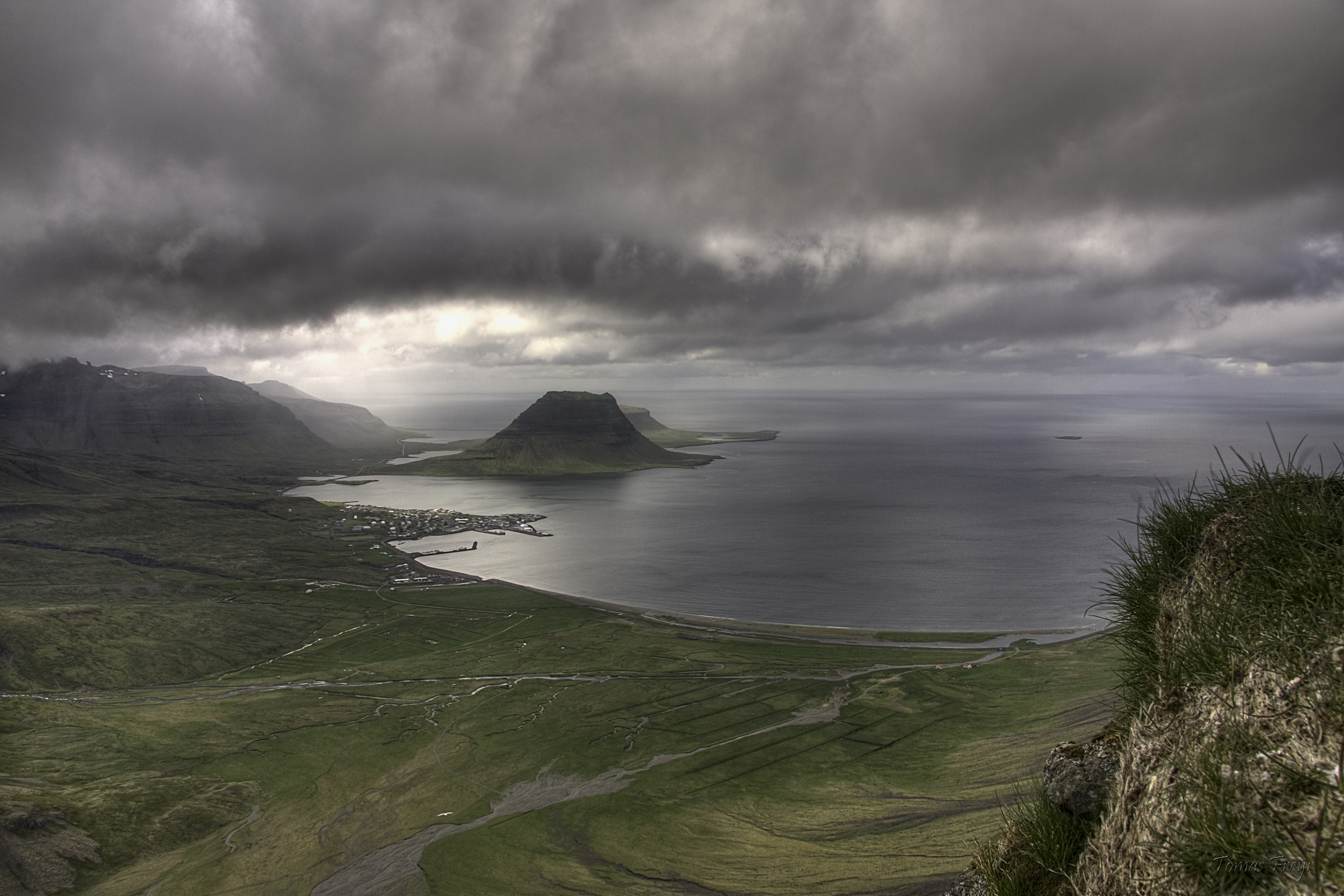 High overlook above Grundarfjörður showing the town, fjord, and Kirkjufell under dark cloud.