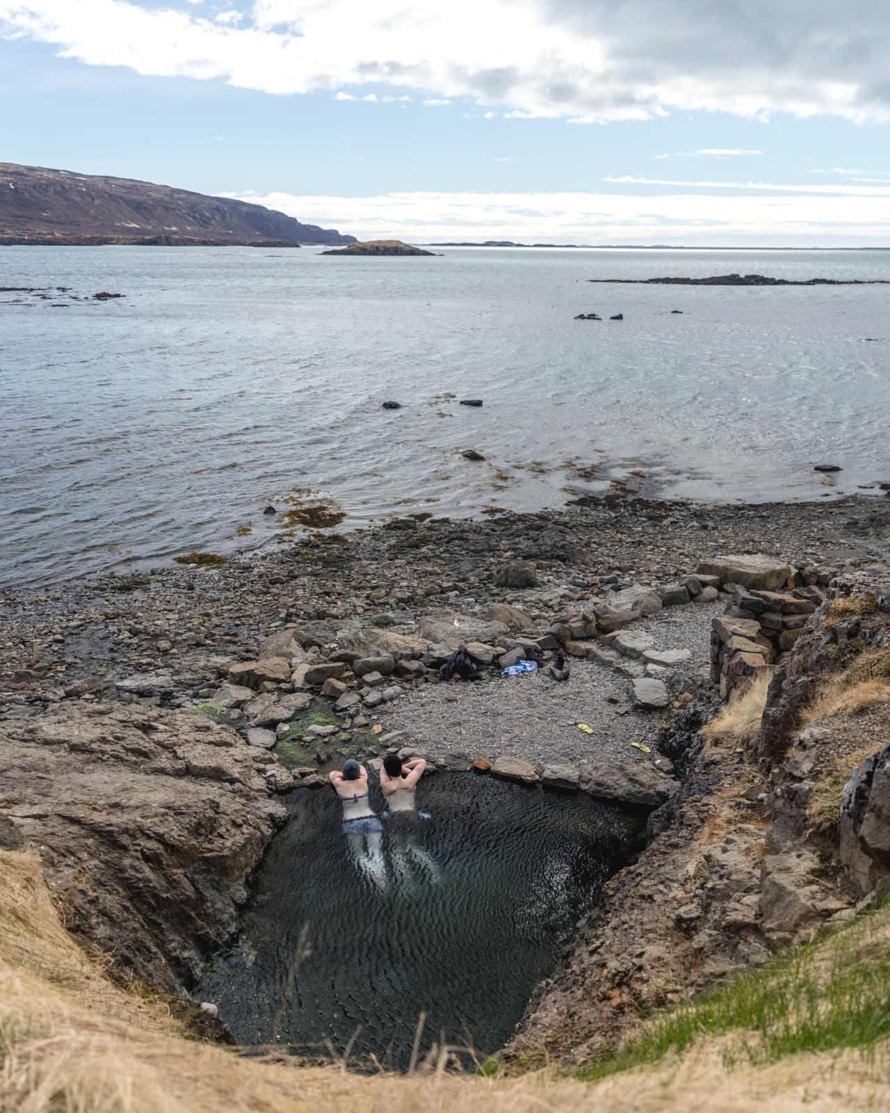Hellulaug seen from above with the hot pool tucked below rocks near the fjord shore.