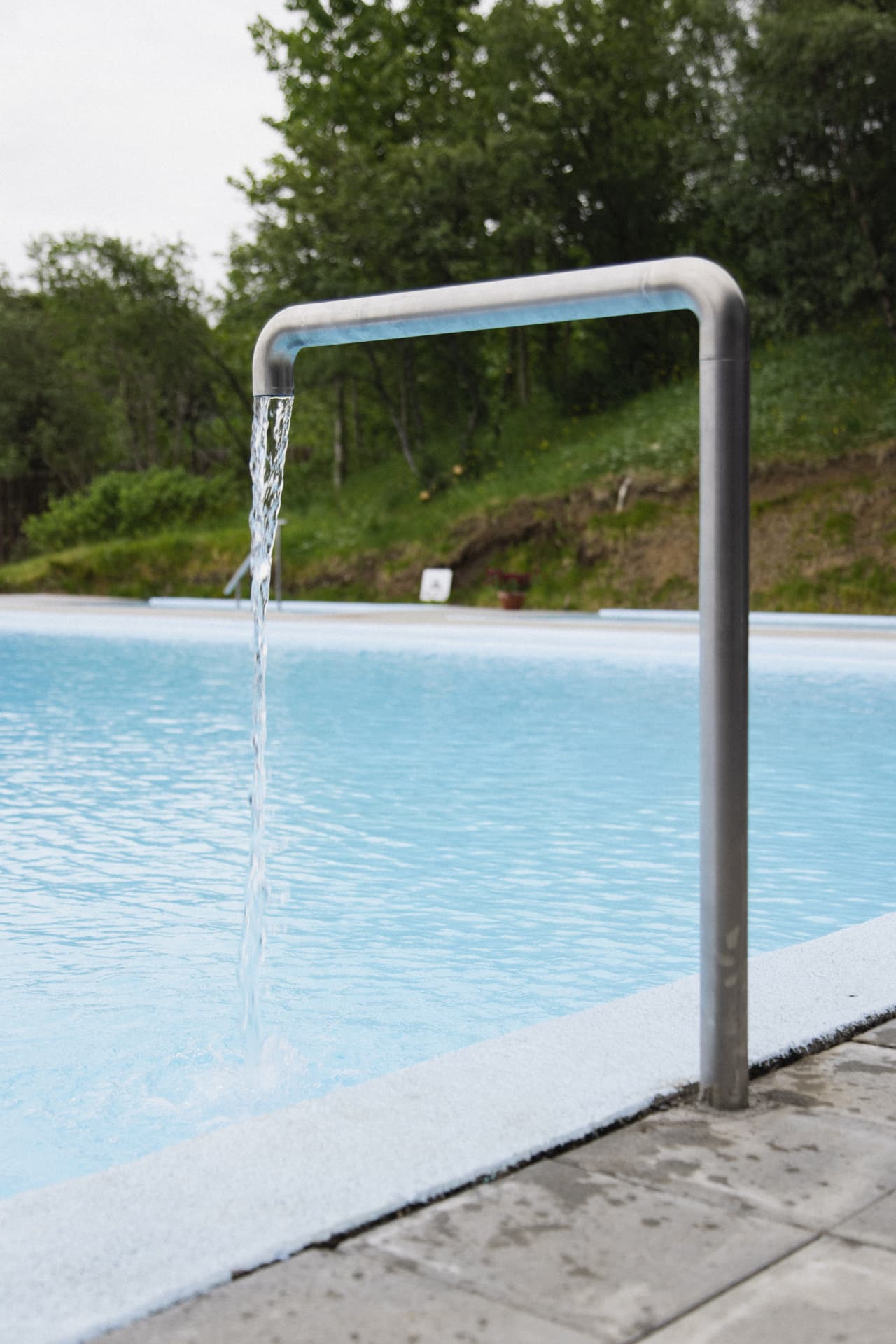 Water flowing from a metal pipe into the blue water at Hreppslaug Pool.