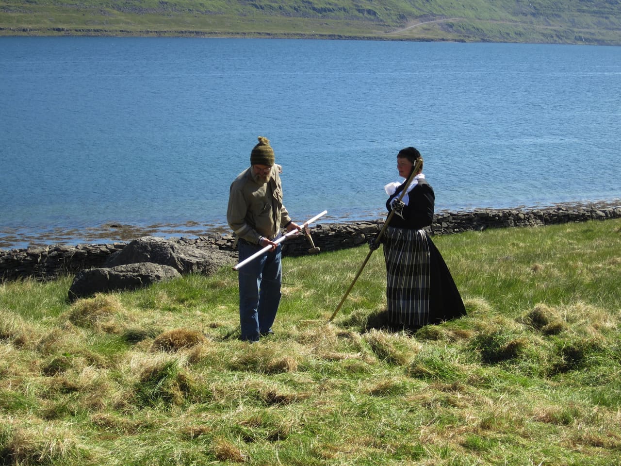 People in traditional clothing on the grass near Litlibær with Skötufjörður water behind them.