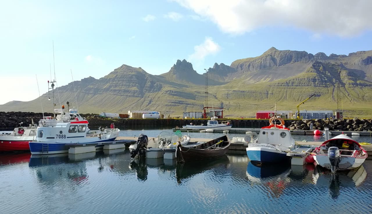 Fishing and small harbor boats in Stöðvarfjörður with the mountain wall rising directly behind the village.