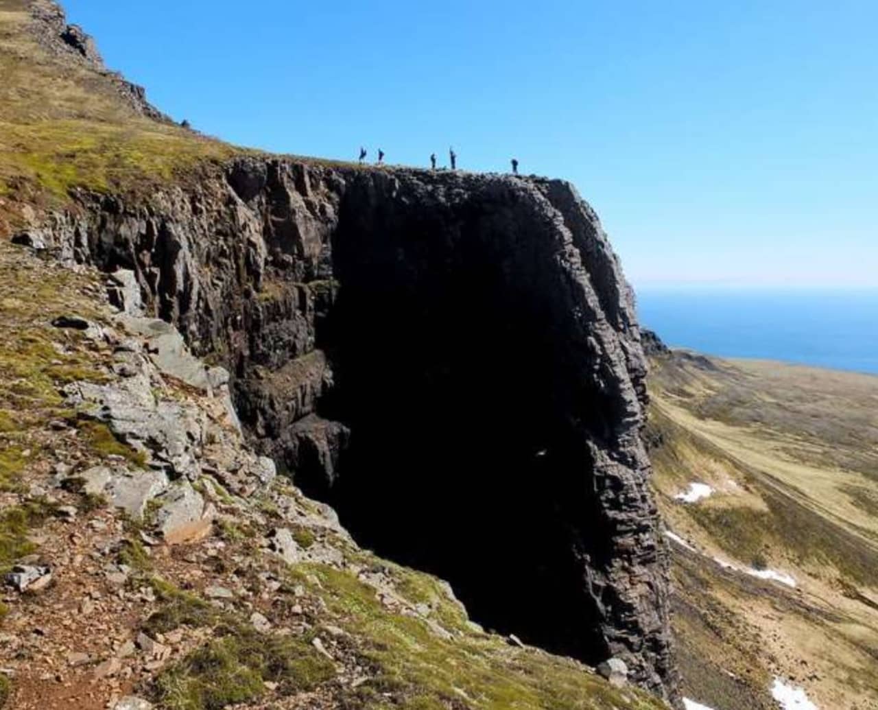 Cliffside view at Stórakerald and Tyrkjaurð above Stöðvarfjörður with hikers standing on the ridge.