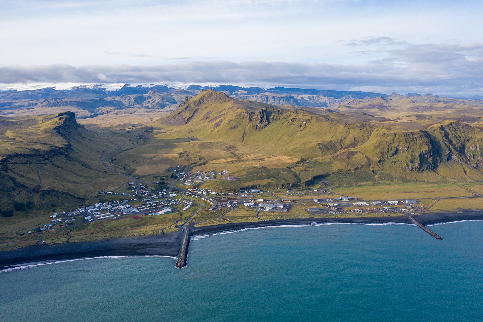 Aerial view of Vík showing the village, black-sand shore, and steep South Coast slopes.