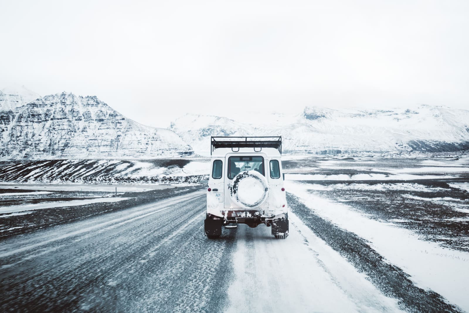 Vehicle driving through snowy mountains on an icy Iceland road.