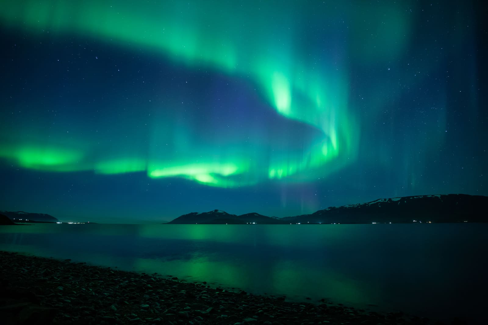 Northern lights over dark Icelandic mountains and water.