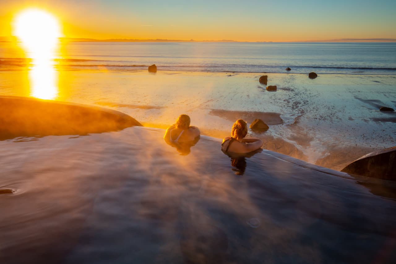 Guðlaug hot pool above Langisandur beach in Akranes with the sea and mountains beyond.