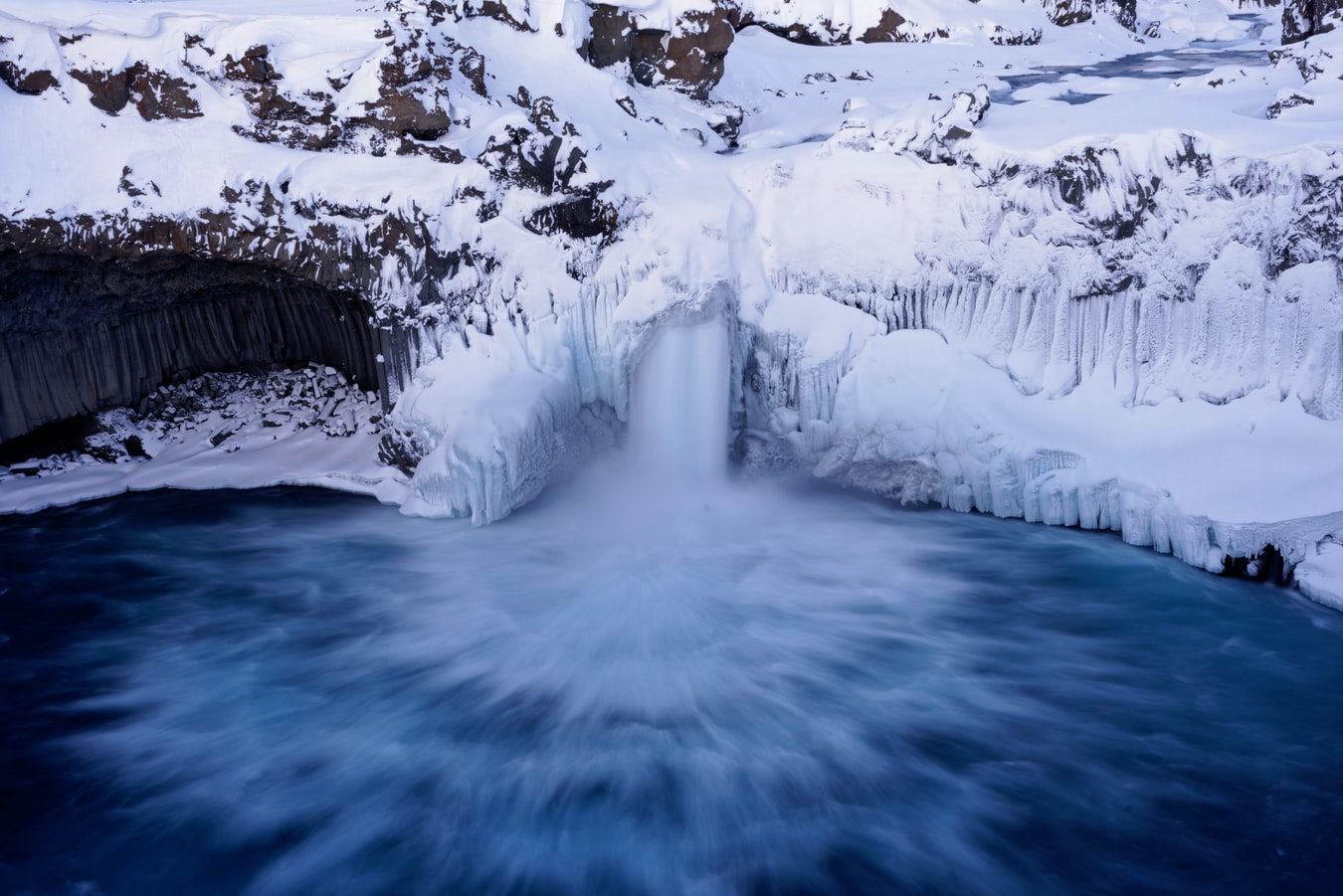 Aldeyjarfoss in winter with snow and ice clinging to the basalt around the waterfall.