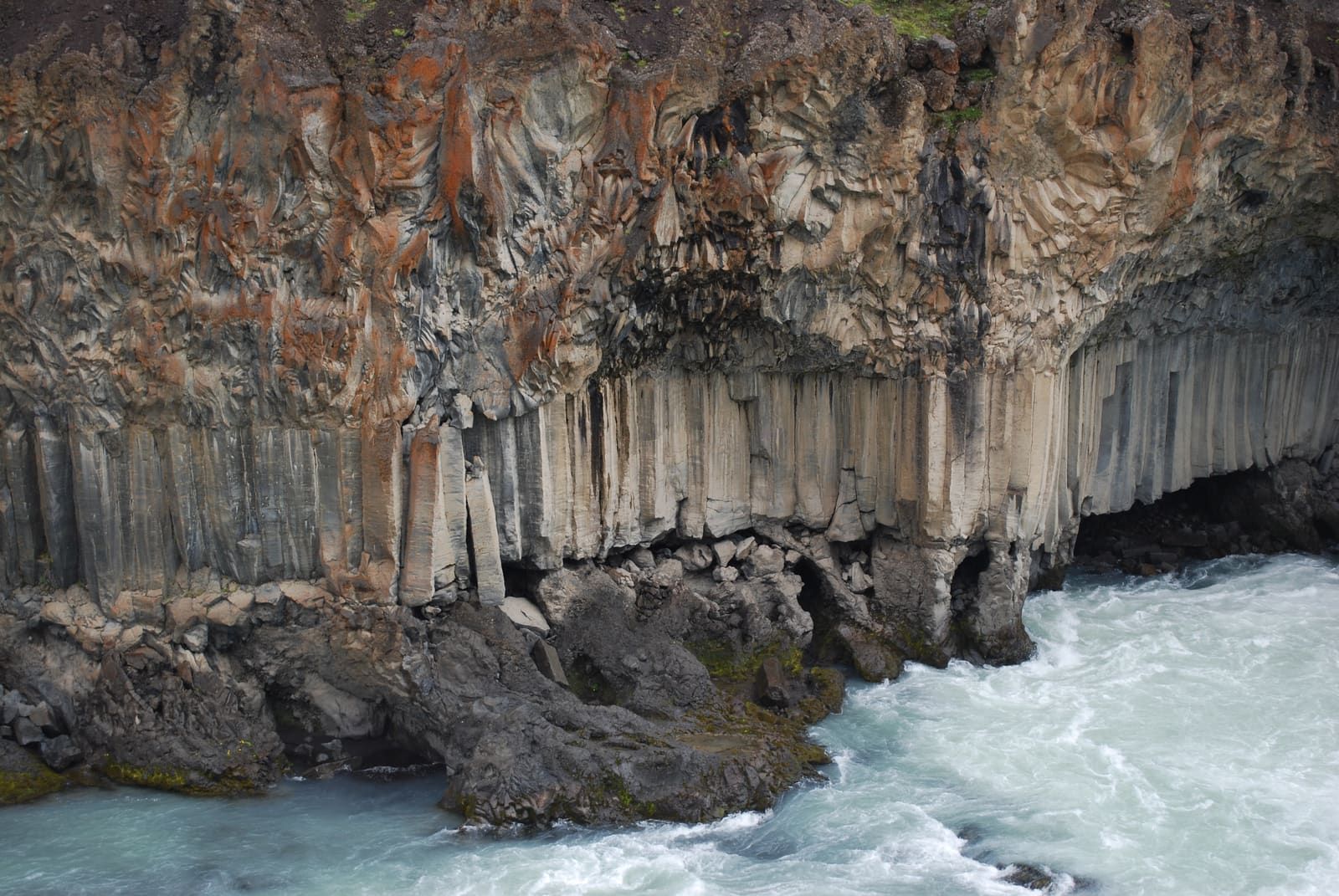 Close view of layered basalt columns beside the pale river at Aldeyjarfoss.